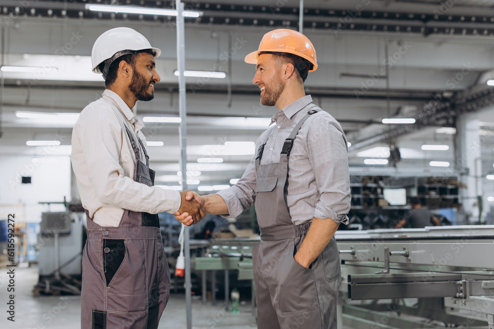 Two international male workers in overalls shake hands against the background of the production of PVC windows and doors Two international male workers in overalls shake hands against the background of the production of PVC windows and doors