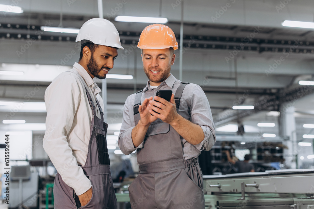 Two international male workers in overalls looking at the phone against the background of the production of aluminum PVC windows and doors Two international male workers in overalls looking at the phone against the background of the production of aluminum PVC windows and doors