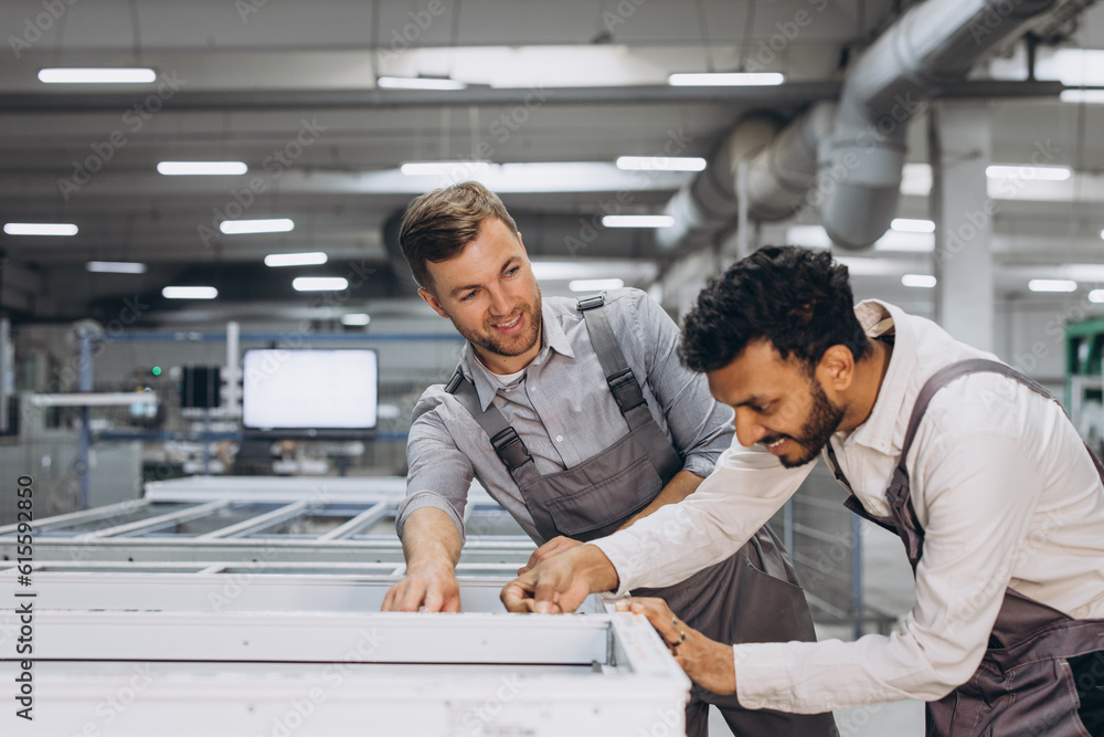 Obraz premium Two male international workers in overalls work together at a machine for the production of aluminum PVC windows and doors