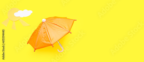 Small umbrella, paper cloud and sun on yellow background with space for text