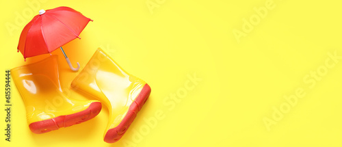 Gumboots and mini umbrella on yellow background with space for text
