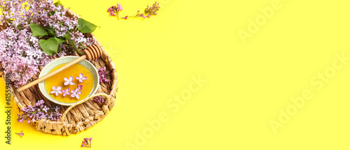Wicker tray with lilac flowers and sweet honey on yellow background with space for text