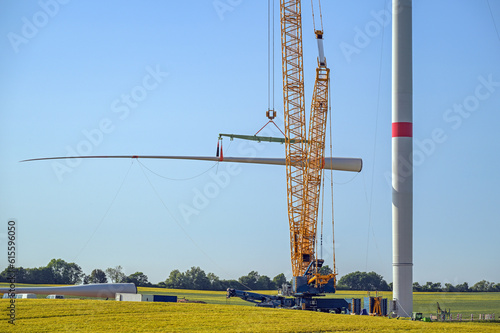 Wind turbine construction site, crane is lifting a blade to install it onto the tower, heavy industry for electricity, renewable energy and power, rural landscape, blue sky, copy space, selected focus