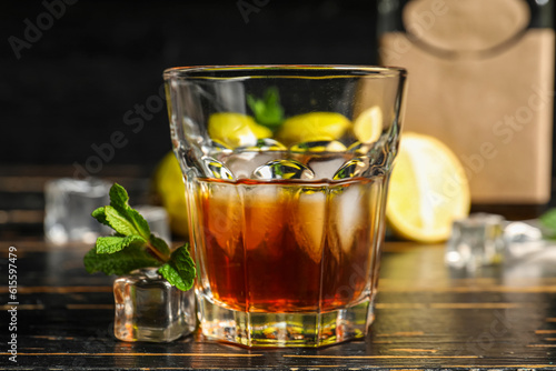 Glass of rum with ice cubes on dark wooden background, closeup