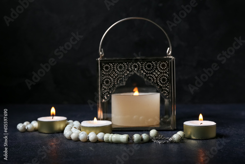 Muslim lamp with burning candles and prayer beads on dark background