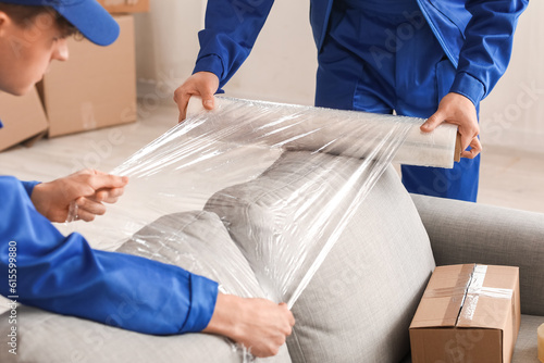 Obraz na płótnie Male movers wrapping sofa with stretch film in room, closeup