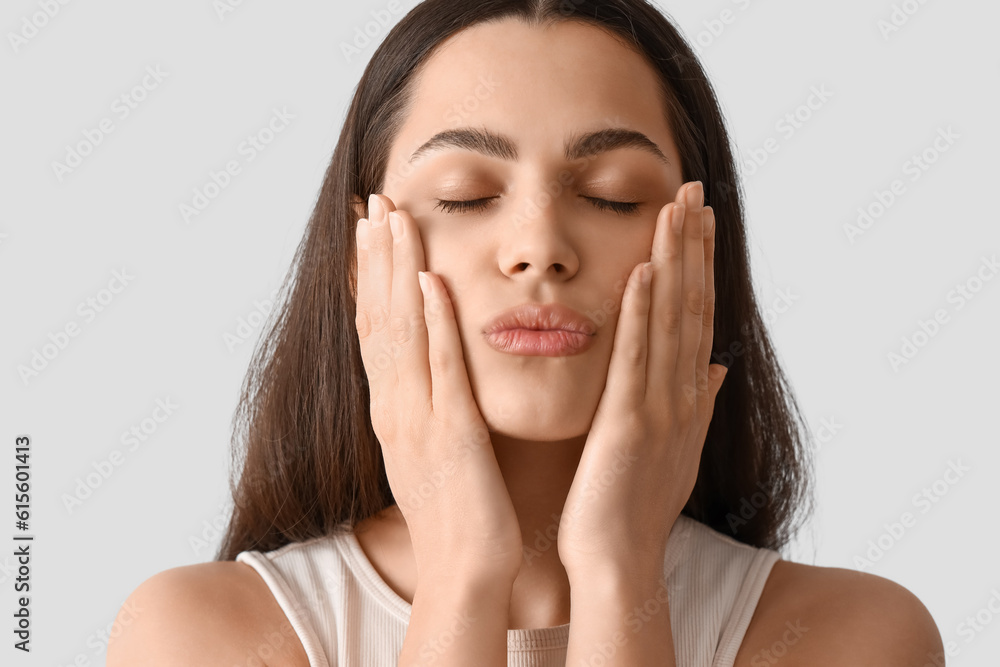 Young woman doing face building exercise on light background, closeup Young woman doing face building exercise on light background, closeup
