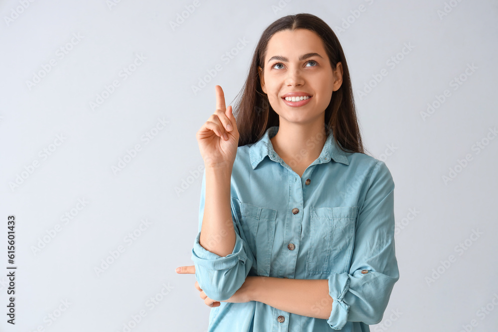 Thoughtful young woman pointing at something on light background Thoughtful young woman pointing at something on light background