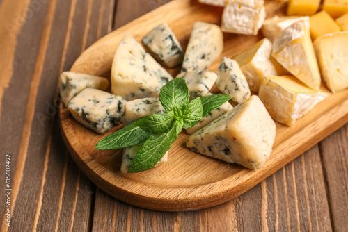Board with pieces of tasty cheese on wooden background, closeup