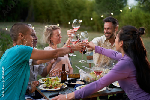 Happy friends having fun drinking red wine on backyard at private dinner party. Middle-aged people eating bbq food at restaurant together. Dining lifestyle concept. Focus on glasses. High quality