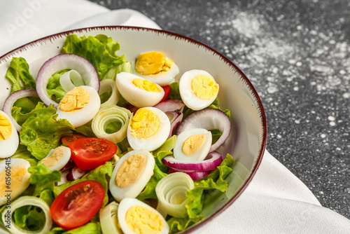 Tasty salad with quail eggs, tomatoes, onion and lettuce on dark grunge background, closeup