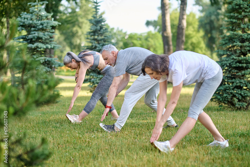 Mature group of people exercising outdoors, healthy lifestyle, stretching body before workout