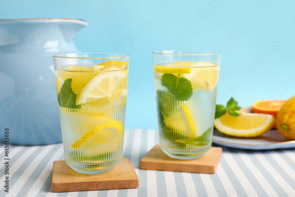 Glasses and jug of infused water with lemon and mint on blue background Glasses and jug of infused water with lemon and mint on blue background