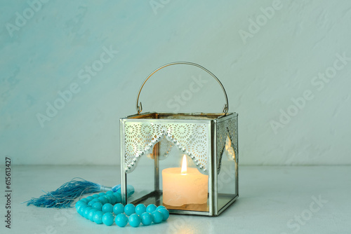 Fanous with burning candle and tasbih on light background. Islamic New Year celebration photo