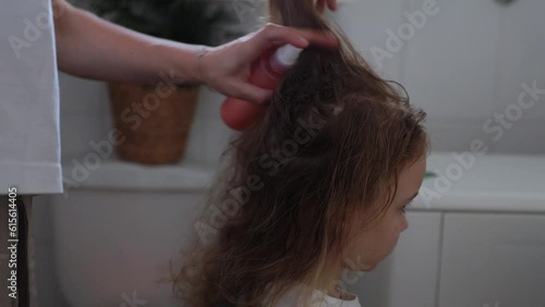 A woman helps to get rid of lice and parasites on the head of a little girl, combs her head with a special comb. Treatment of lice and nits photo