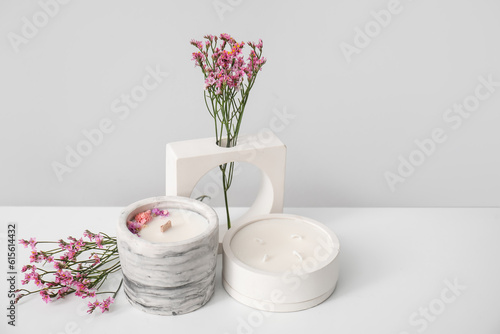 Beautiful flowers and candles on table near light wall in room  closeup