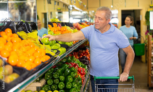 Foto Portrait of focused elderly casual man buying fresh local green apples in grocer