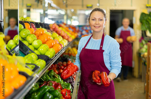 Positive middle-aged woman market assistant arranging organic bell pepper in grocery shop