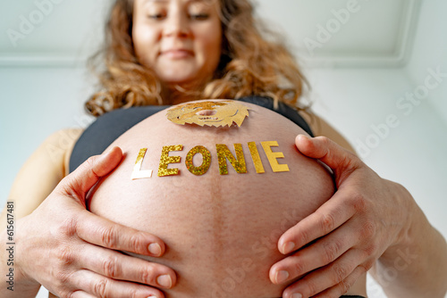 Baby bump shot with glittering lion sticker and child name from below of laughing pregnant woman at home. Last month of pregnancy - week 36. White background. photo