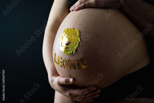 Baby bump shot with glittering lion sticker and child name from the side of pregnant woman at home. Last month of pregnancy - week 36. Black background. photo