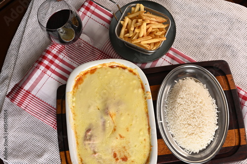 bolognese lasagna baked with cheese ham red sauce spices and meat with french fries and rice.