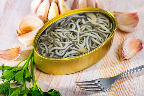 Obraz na plátně Open tin can of pickled eels and garlic with greens at table, nobody