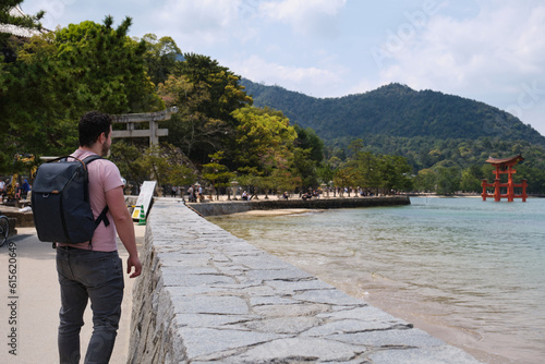 European tourist visiting Itsukushima Jinja Otorii or Grand Torii Gate on the sea of Miyajima, Hiroshima, Japan. photo