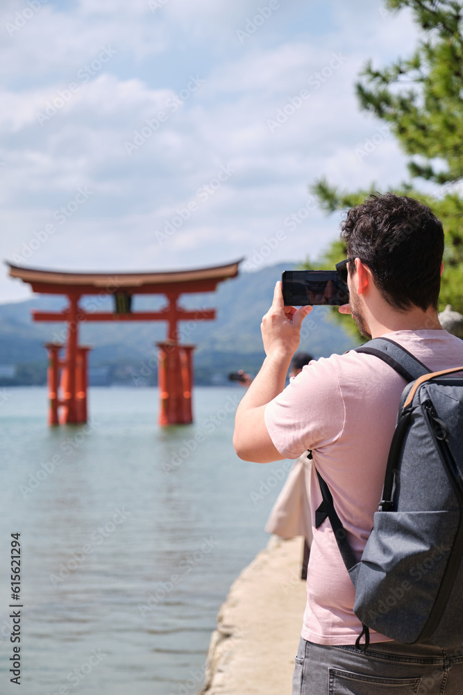 European tourist taking photos of Itsukushima Jinja Otorii or Grand Torii Gate on the sea of Miyajima, Hiroshima, Japan.