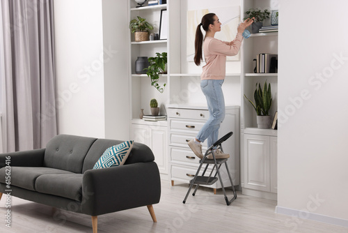 Woman on ladder watering houseplant at home