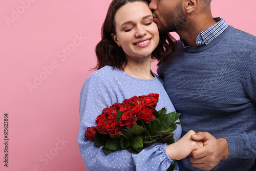 Happy couple celebrating Valentine's day. Beloved woman with bouquet of red roses on pink background, space for text