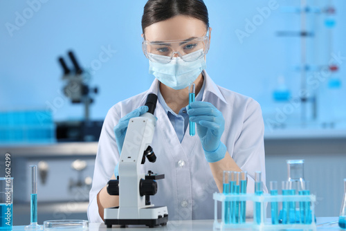 Scientist holding test tube with light blue liquid and microscope in laboratory