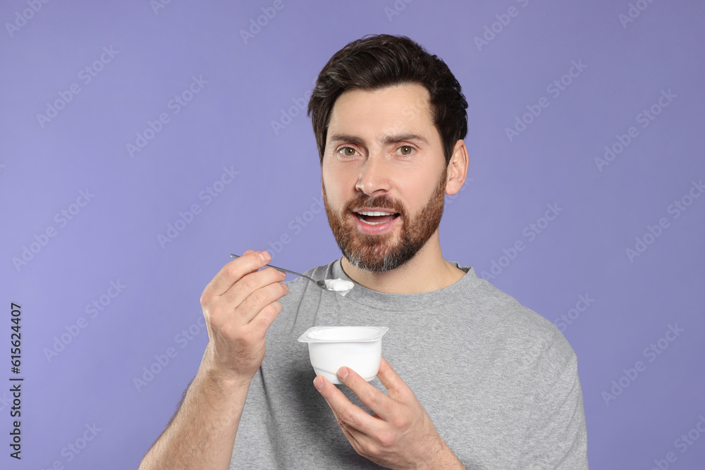 Handsome man eating delicious yogurt on violet background Handsome man eating delicious yogurt on violet background