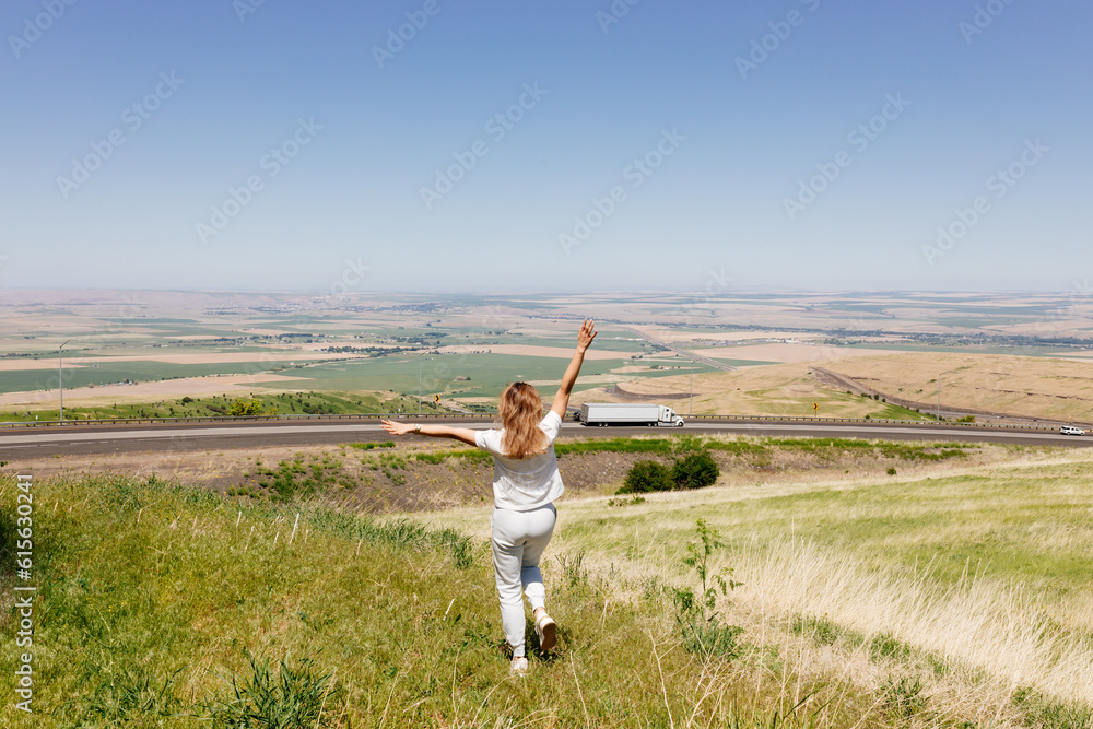 Fototapeta premium Beautiful summer landscape with meadows and a road from a bird's eye view. Nature in Oregon. A girl in sportswear with red hair walks in a summer meadow, rests in nature, admires nature