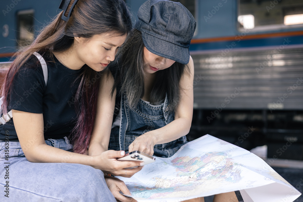 Two female sitting with map choose where to travel and bag waiting for train at train station. Two female sitting with map choose where to travel and bag waiting for train at train station.