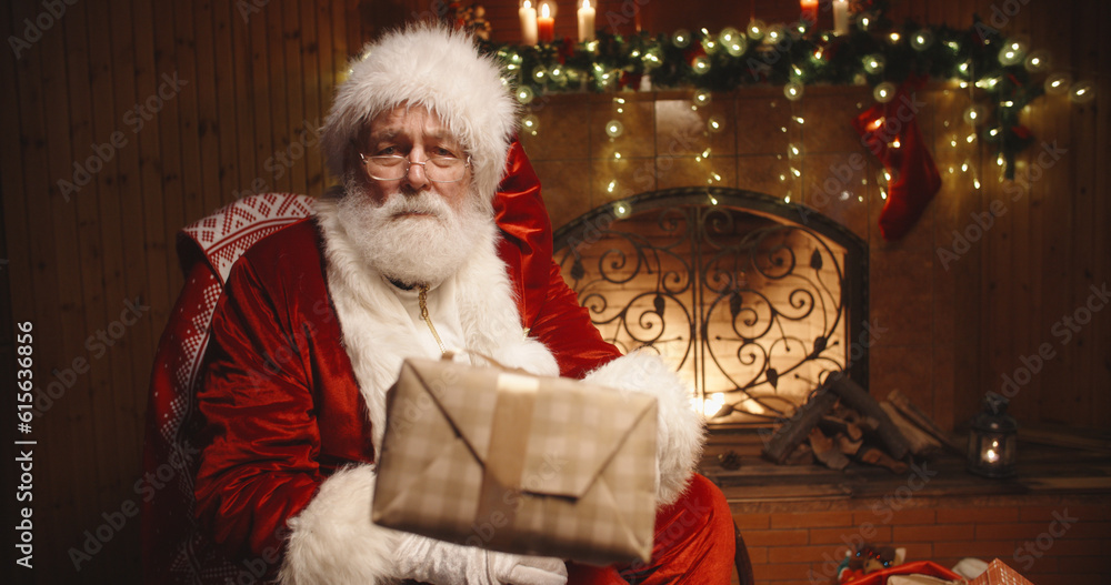 Merry Christmas and Happy Holiday. Santa Claus with christmas present looking at camera . Winter night with snowfall
