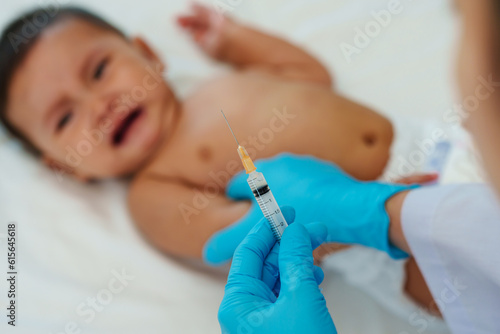 doctor holding syringe and preparing vaccine giving injection to arm of crying baby