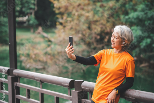 Elderly white haired Asian woman talking Video call while exercising in the park in the morning.