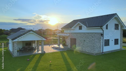 Aerial view approaching a modern family house in a neighborhood, during sunset