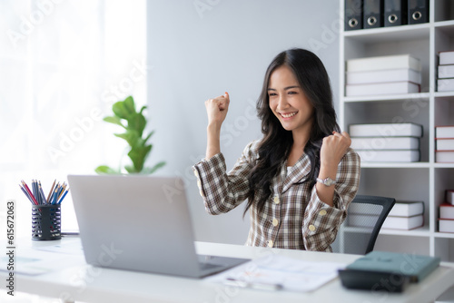 Happy asian businesswoman raising hands with victory smiling happily with laptop computer. The concept of success at work.