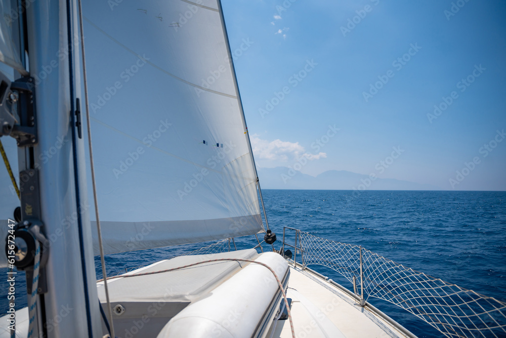 Obraz premium Yacht sailing in an open sea. Close-up view of the deck, mast and sails. Clear sky, waves and water splashes