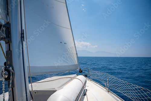 Yacht sailing in an open sea. Close-up view of the deck, mast and sails. Clear sky, waves and water splashes