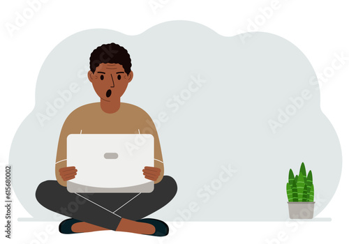 A man sits cross-legged in his hands holding a laptop. The concept of work, education, reading, watching videos.