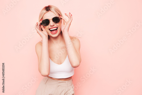 Young beautiful smiling blond female in trendy summer white top t-shirt and beige trousers clothes. Sexy carefree woman isolated on pink background in studio. Positive model. In sunglasses © halayalex