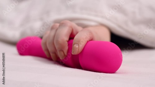 Woman taking pink vibrator lying under white blanket.  photo