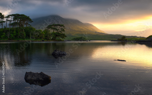 Dramatic cloudy sunrise lakeside landscape scenery of twelve pines island reflected in water surrounded by mountains at Derryclare, connemara national Park in County Galway, Ireland 