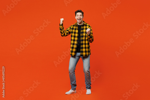 Full body young happy man he wear yellow checkered shirt black t-shirt doing winner gesture celebrate clenching fists say yes isolated on plain red orange background studio portrait Lifestyle concept