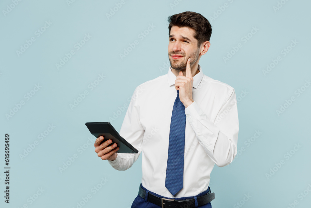 Young minded puzzled successful employee business man corporate lawyer wearing classic formal shirt tie work in office using calculator isolated on plain pastel light blue background studio portrait. Young minded puzzled successful employee business man corporate lawyer wearing classic formal shirt tie work in office using calculator isolated on plain pastel light blue background studio portrait.