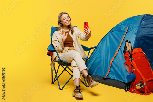 Full body young woman sit near bag stuff tent do selfie shot mobile cell phone isolated on plain yellow background. Tourist active lifestyle walk on spare time. Hiking trek rest travel trip concept.