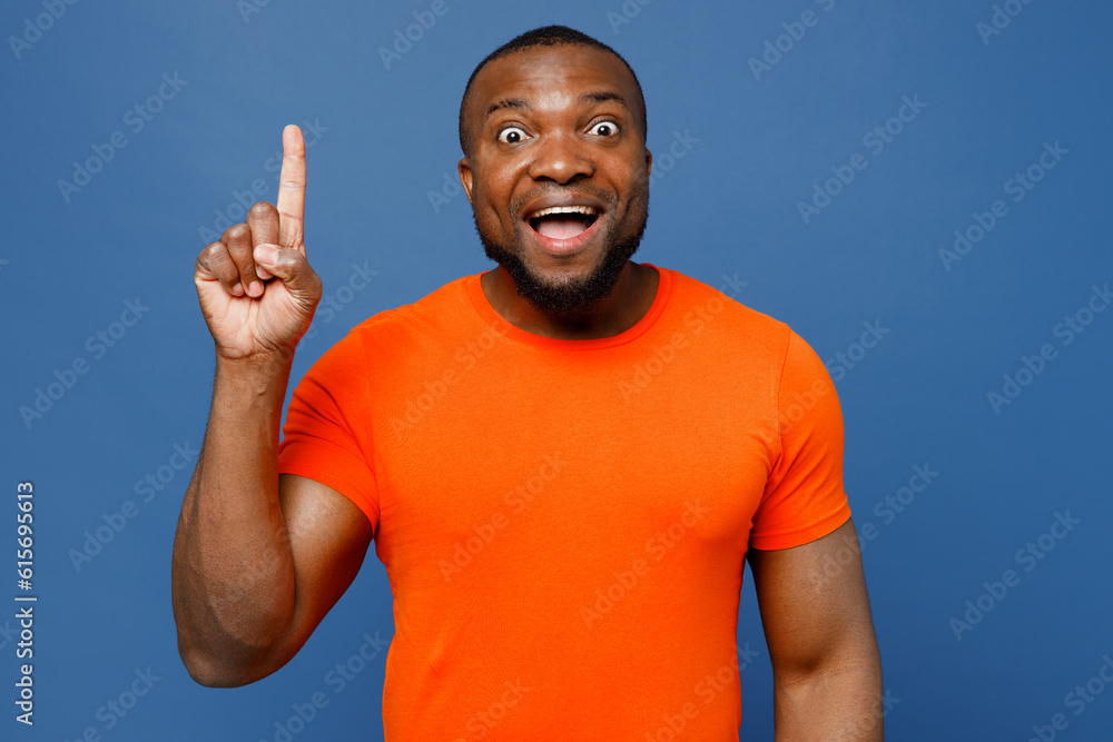 Young insighted man of African American ethnicity wear orange t-shirt holding index finger up with great new idea isolated on plain dark royal navy blue background studio portrait. Lifestyle concept. Young insighted man of African American ethnicity wear orange t-shirt holding index finger up with great new idea isolated on plain dark royal navy blue background studio portrait. Lifestyle concept.