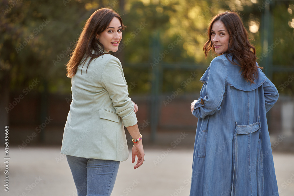 Two women looking back to camera while enjoying a walk outdoors in a park.